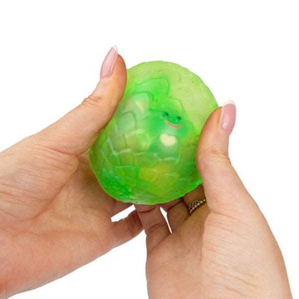 Green turtle-shaped squishy egg held between fingers on a white background.