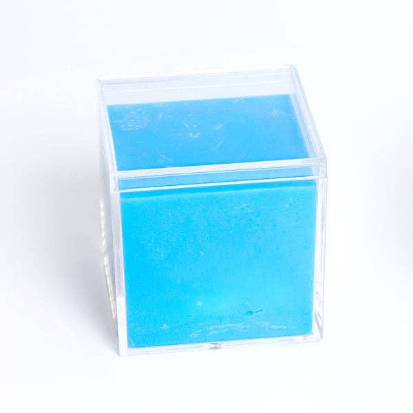 A bright blue rectangular solid product, possibly wax or soap, displayed inside a clear acrylic cube container on a white background.
