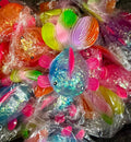 A pile of colorful, glittery fish-shaped squishies wrapped in clear plastic bags. The central fish is blue with pink fins and a multicolor tail, surrounded by other similarly packaged fish in various colors.
